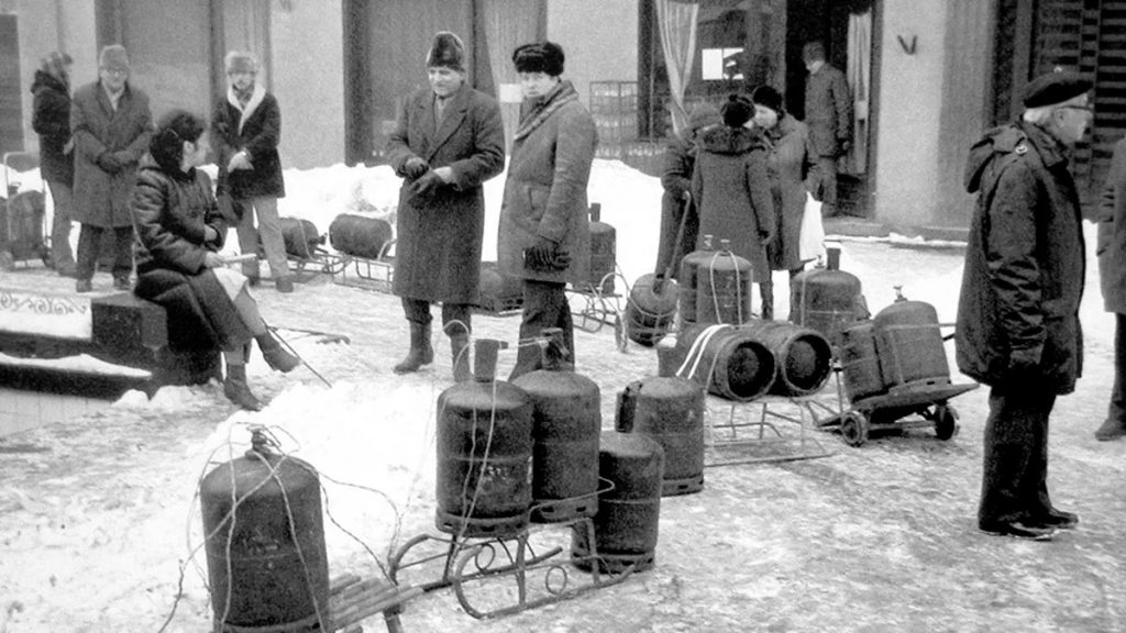 Persone avvolte in coperte attendono nella neve accanto a file di bombole di gas, in una fredda notte della Romania comunista.
