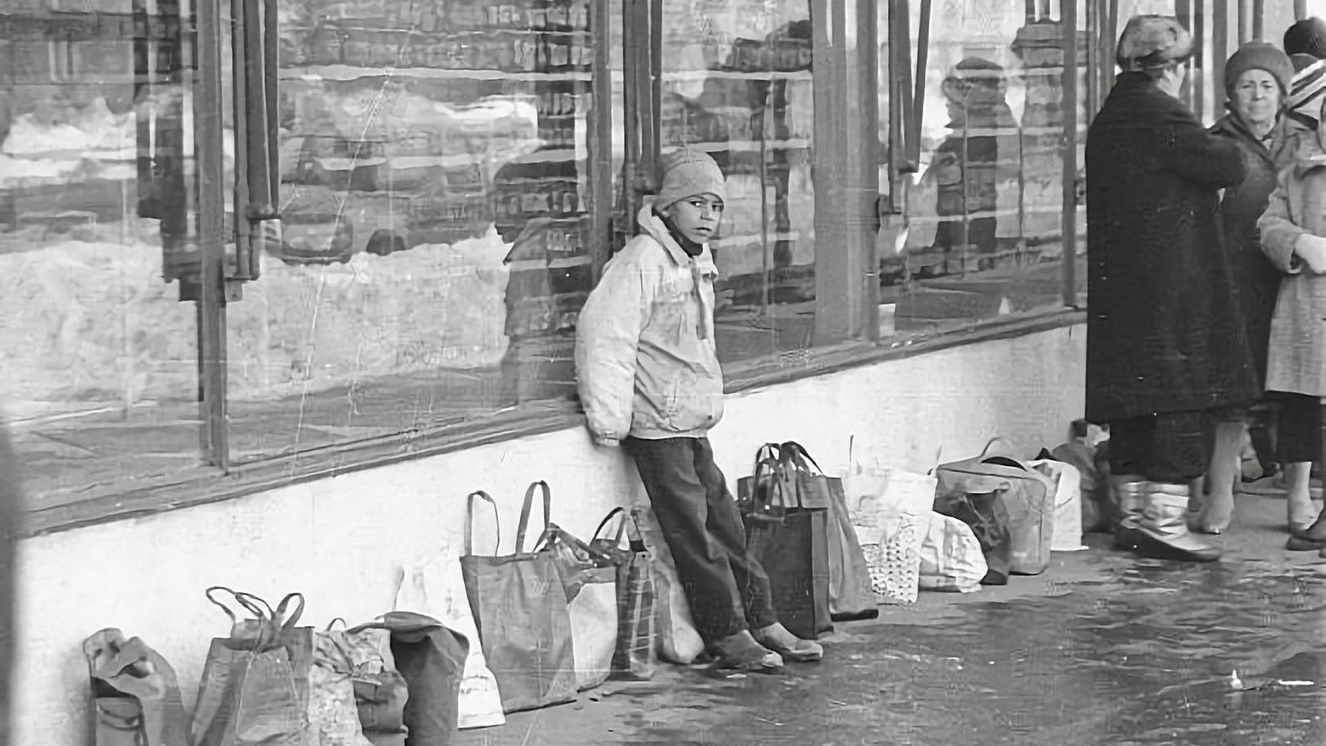 Persone in fila all’alba davanti a un negozio nella Romania comunista, con bottiglie e borse per il latte, immerse nel freddo invernale.