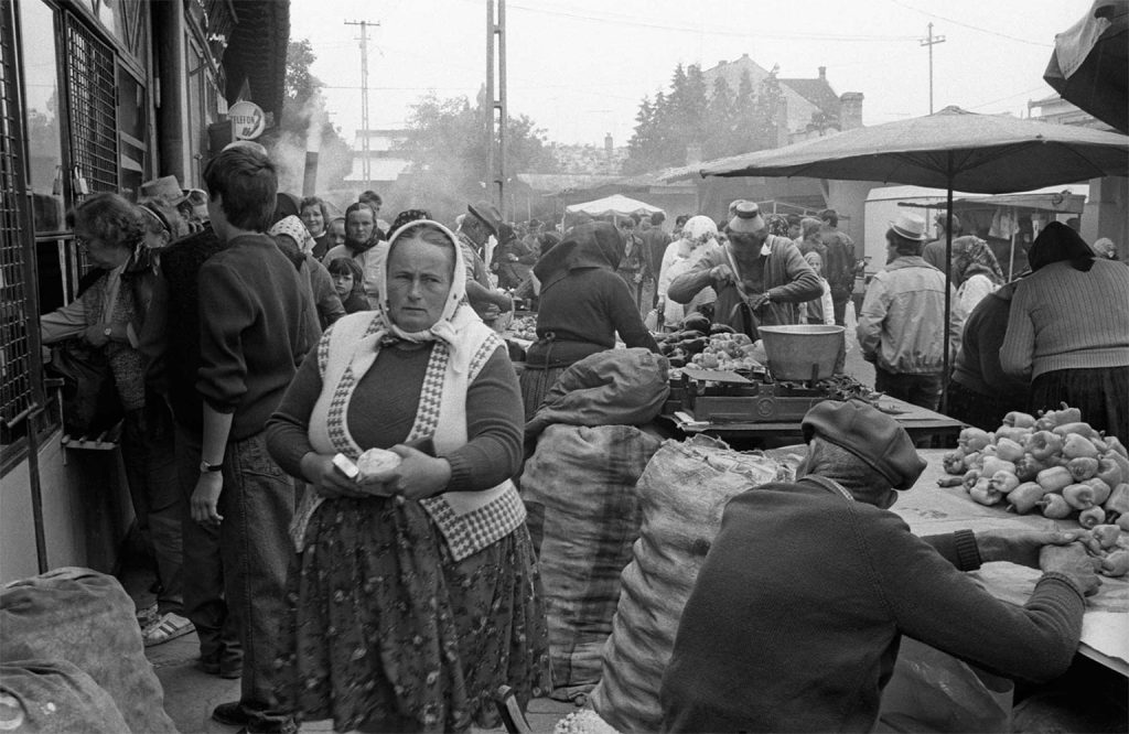 Mercato popolare in Romania durante la crisi economica dopo il 1989, con persone che cercano di vendere e acquistare beni essenziali per sopravvivere.