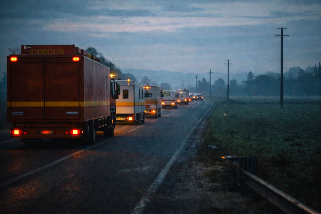 Convoglio di camion e caravan del circo in viaggio all’alba, tappa del percorso di ricostruirsi lontano da casa