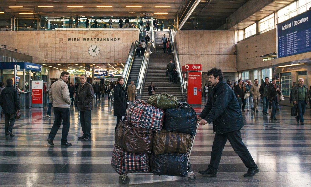 Ritorno in Romania dopo l’emigrazione: uomo con carrello pieno di borse nella stazione di Vienna durante il viaggio