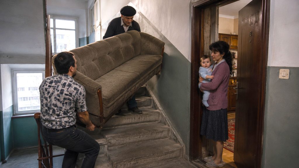 Due uomini trasportano un grande divano sulle scale di un palazzo in Romania nel 1994 durante il ritorno in Romania dopo l’Italia.